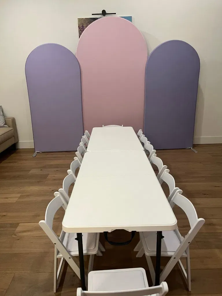 Kids’ rental tables and white chairs set in front of pink and purple party backdrops