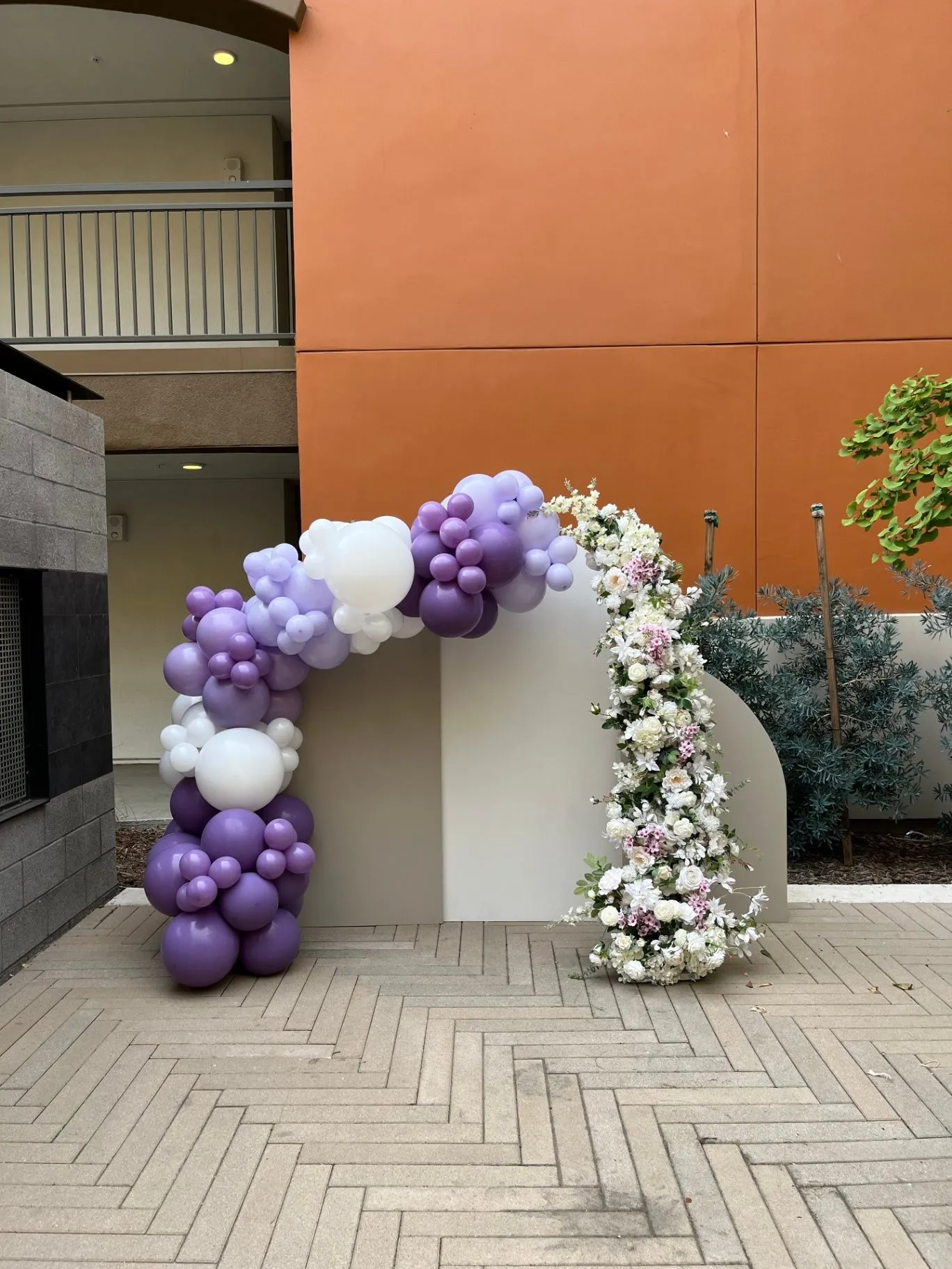 Lavender and white balloon arch with floral accents around a custom event backdrop